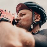 What are the benefits of cycling hats, and how to wear them. Man sipping water from a water bottle wearing a cycling cap.